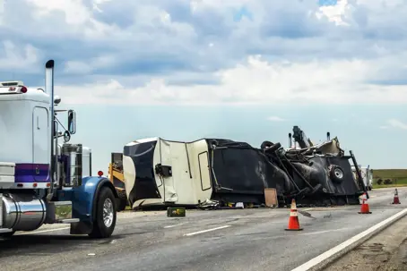 Fifth wheel RV overturned on highway with wench truck trying to get it off the road and two semis parked nearby and traffic cones keeping traffic away