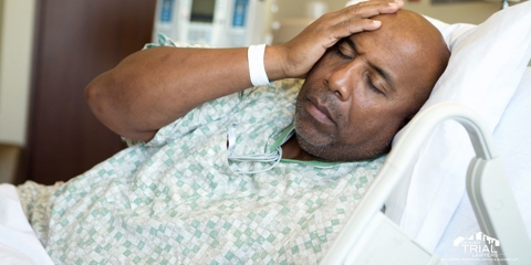 Man in a hospital bed with hand on his head.